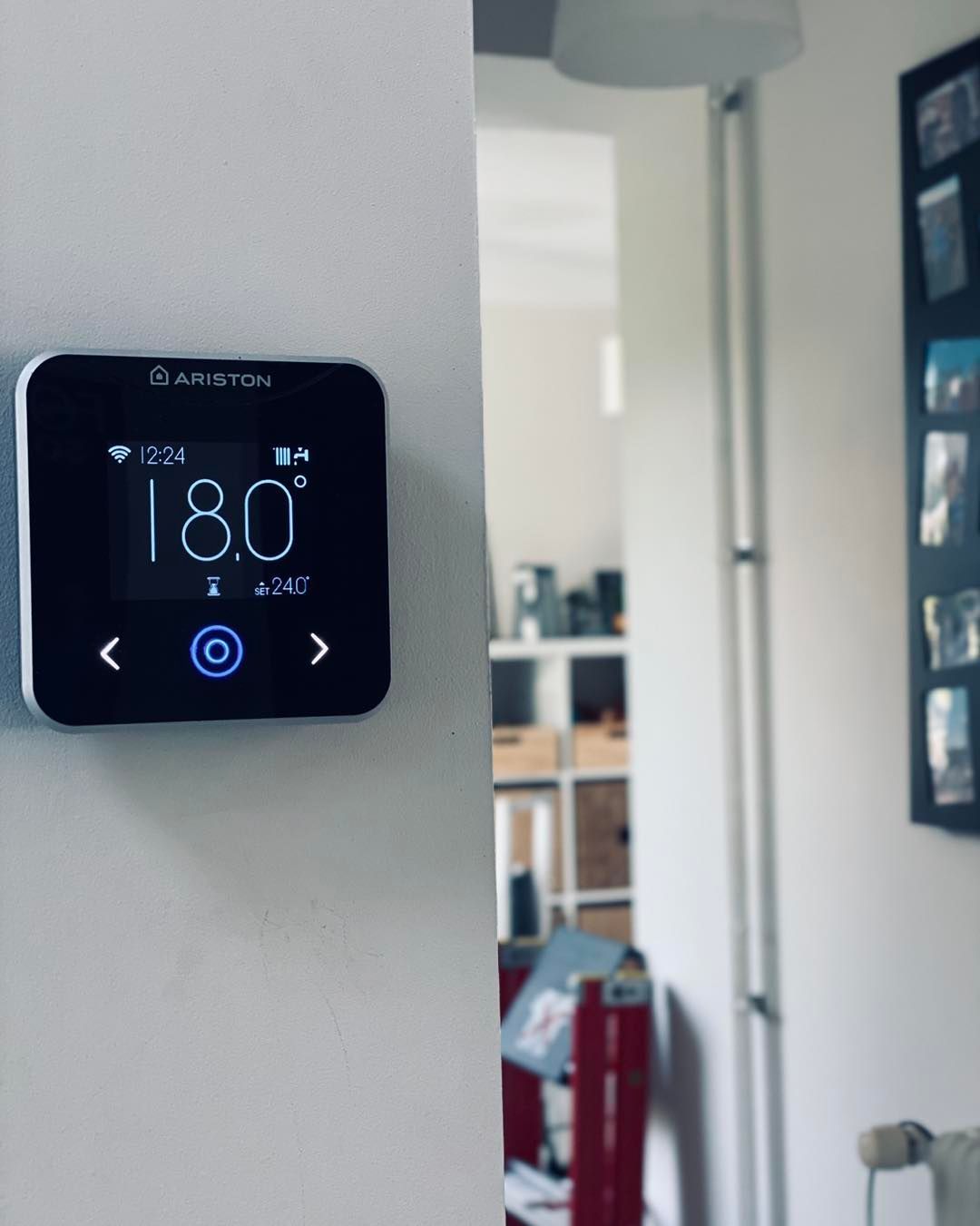 Un thermostat intelligent Ariston, fixé sur un mur blanc.