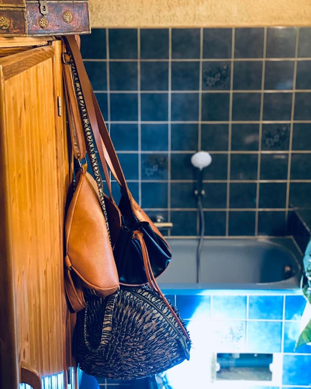 Une personne fixe un pommeau de douche argenté à un tuyau métallique dans une baignoire carrelée de bleu.