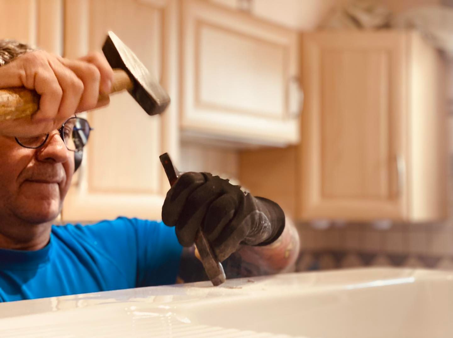Dans une cuisine, une personne utilise un marteau pour enfoncer un burin dans une surface blanche.