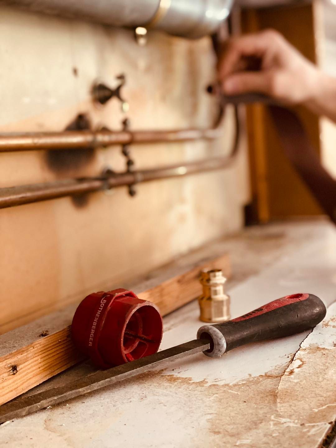 Une personne qui travaille sur des tuyaux de cuivre et des outils sur une étagère, dont un bouchon de tuyau rouge