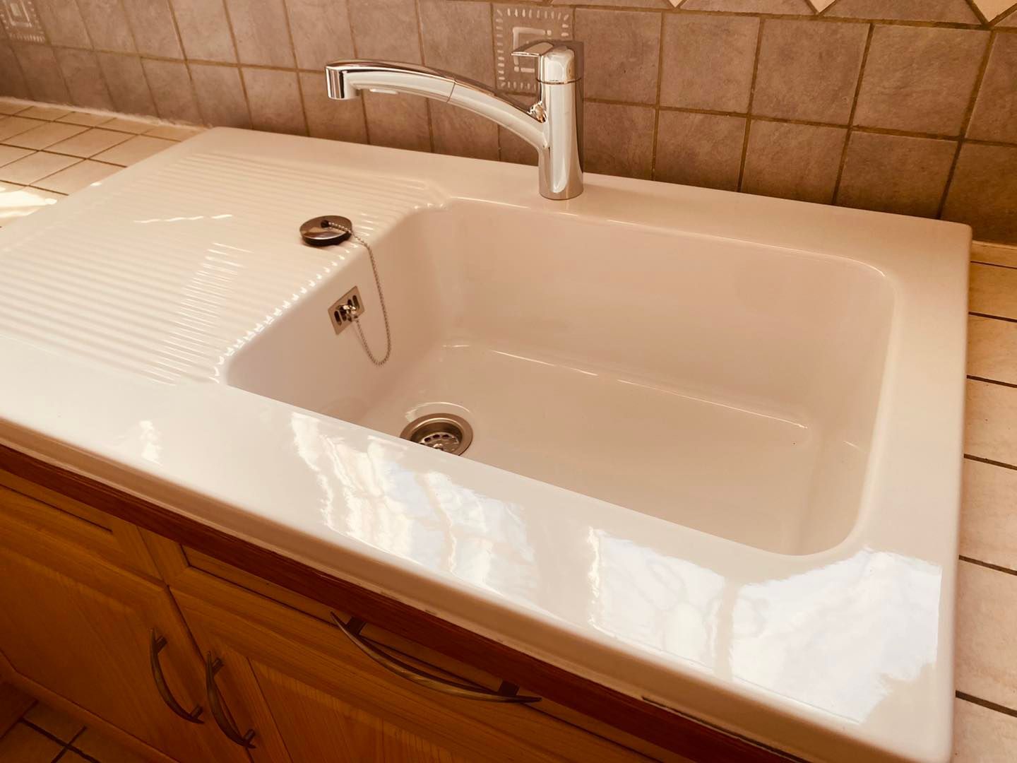 Un évier de cuisine beige clair avec égouttoir et robinet, encastré dans un plan de travail en bois contre un mur carrelé.