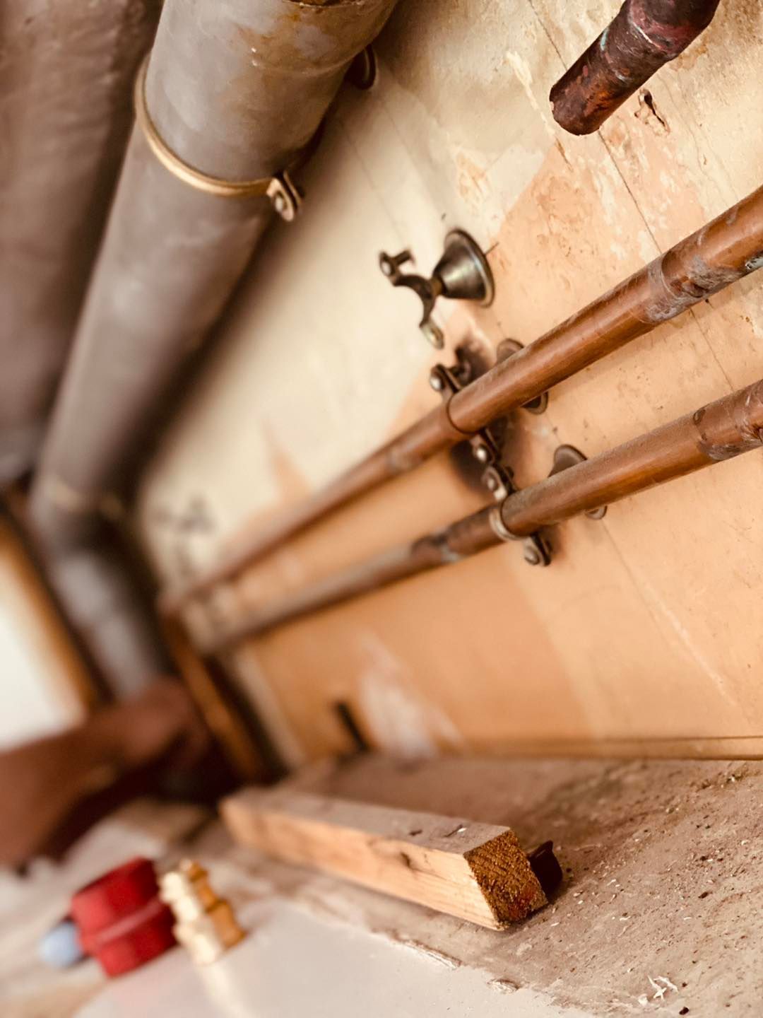 Gros plan sur des tuyaux de plomberie en cuivre et un tuyau d'évacuation gris longeant un mur beige.