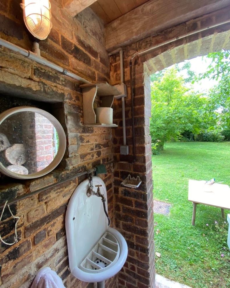 Des mains serrent un pommeau de douche argenté sur un tuyau fixé à un robinet mural, devant des murs carrelés bleu foncé.