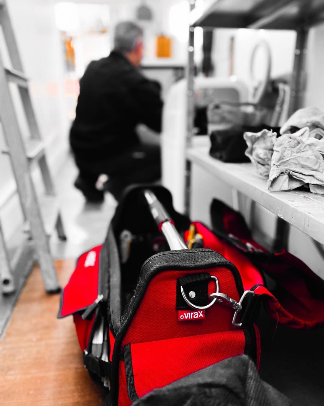 Au premier plan, une sacoche à outils rouge est posée sur un plancher en bois