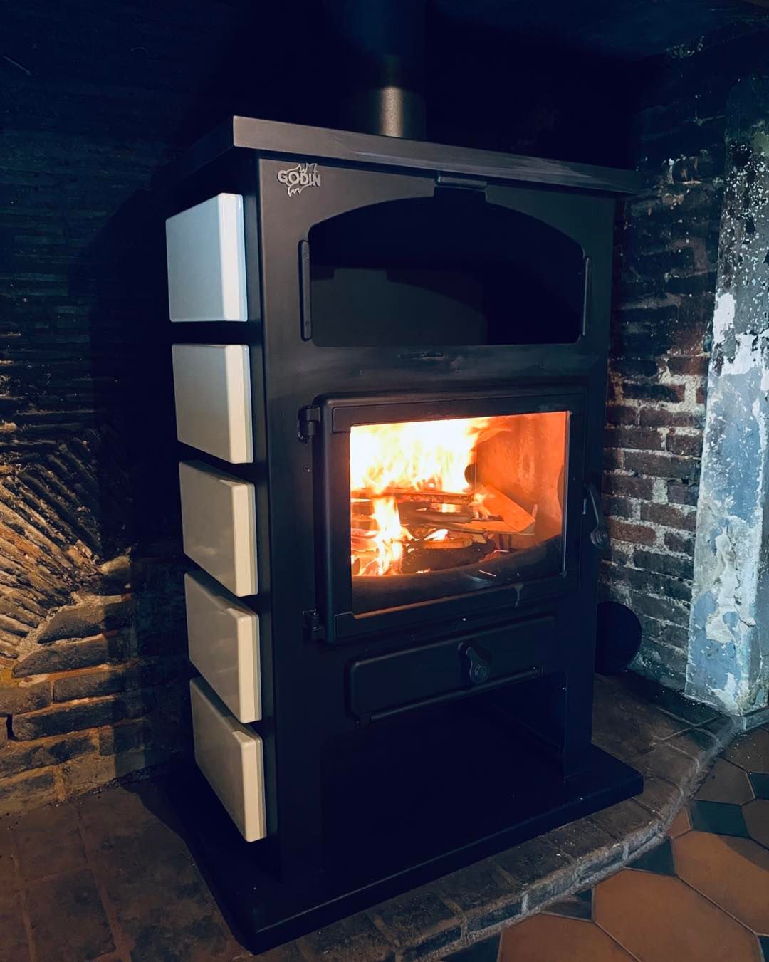 Un poêle à bois noir aux panneaux latéraux blancs brûle 