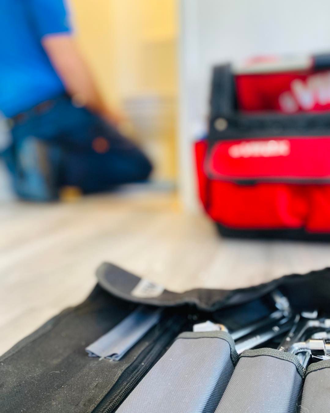 Un professionnel flou en uniforme bleu travaille dans l'embrasure d'une porte, à côté d'une boîte à outils rouge