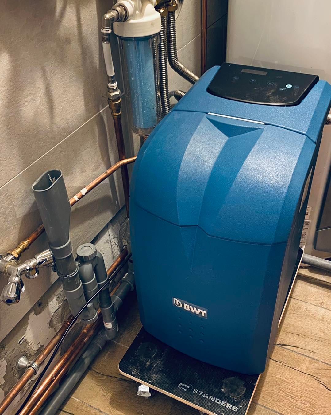 Un adoucisseur d'eau BWT bleu est installé sur une petite plateforme à roulettes