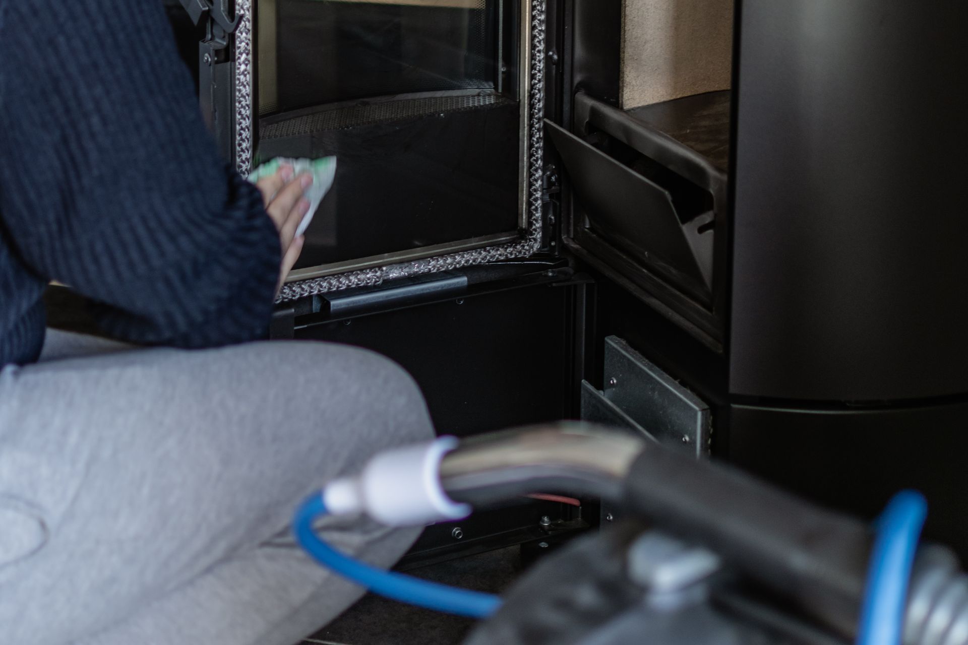 Une personne utilise un chiffon humide pour nettoyer la porte vitrée d'un poêle à bois.