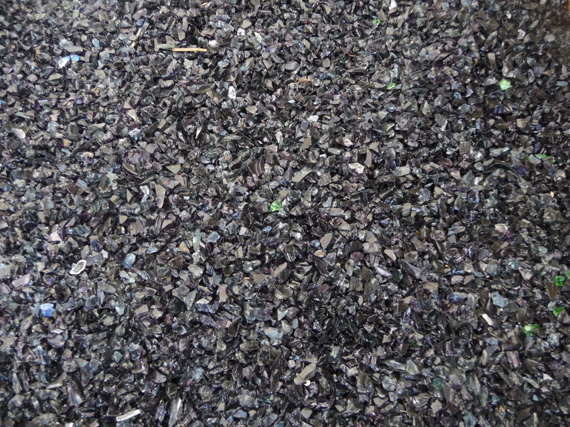 Gros plan sur du gravier gris foncé avec de petites taches vertes éparses.