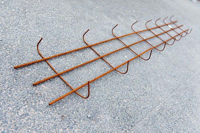 Grille de barres d'armature métalliques rouillées sur un pavé gris, disposée en un long treillis rectangulaire.