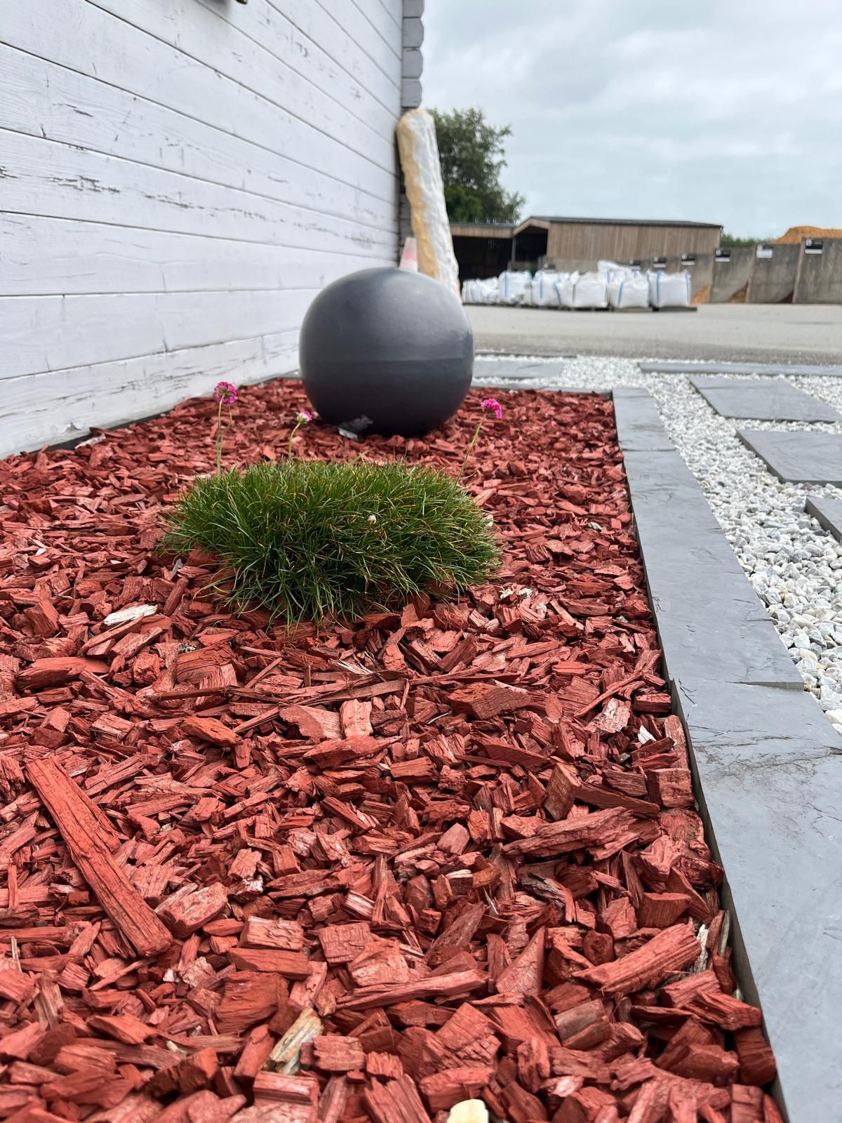 Ornement de jardin sphérique noir à côté d'un mur blanc dans un parterre de paillis rouge