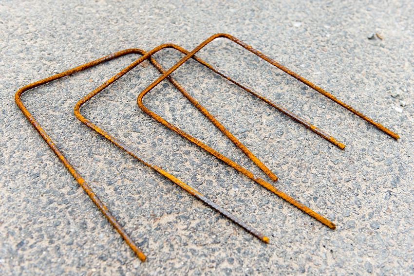 Tuteurs de jardin en métal rouillé gisant sur une surface en béton gris.