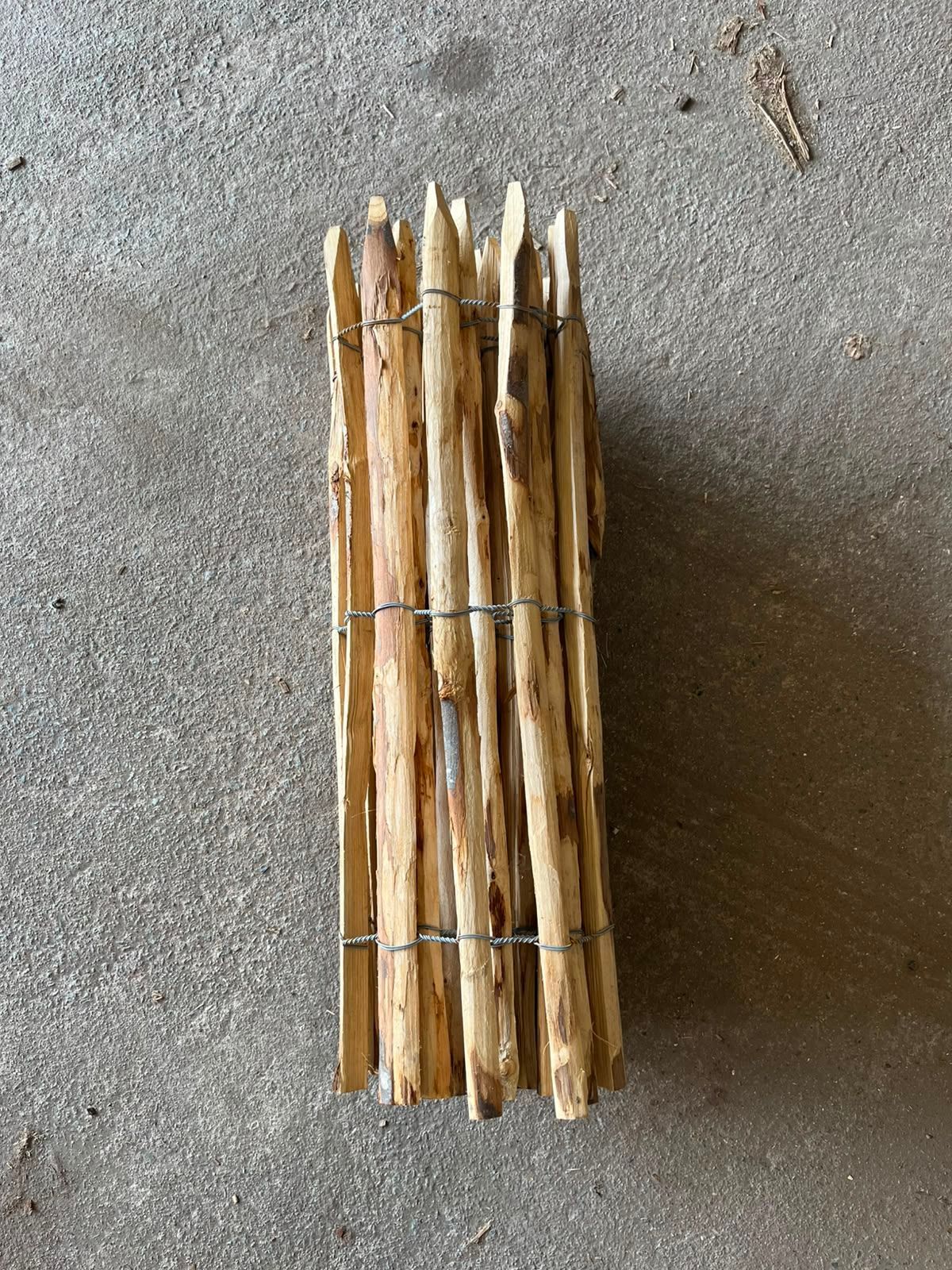 Faisceau de fines baguettes de bois attachées ensemble sur une surface en béton gris.
