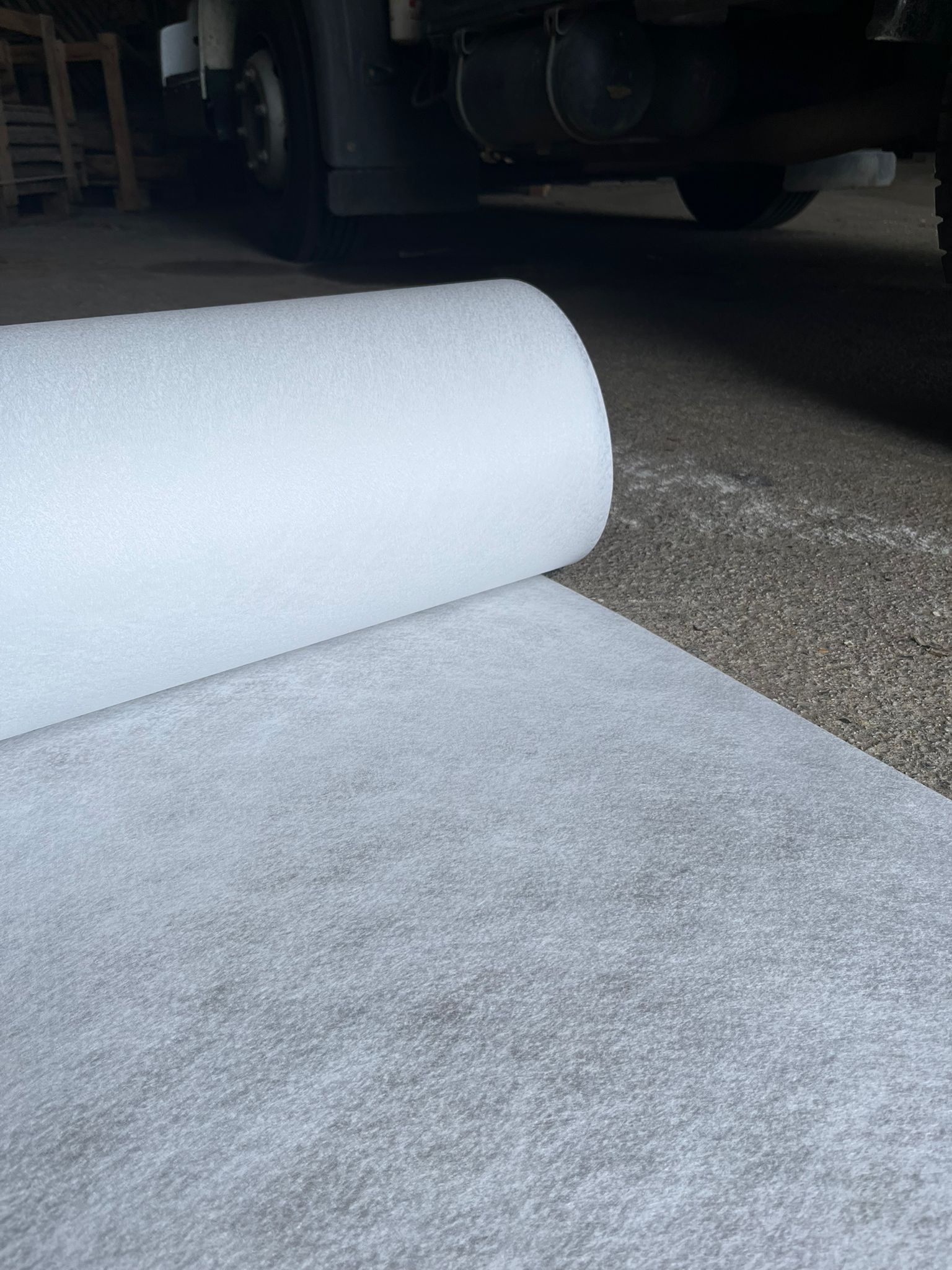 Tapis blanc enroulé, posé sur un sol en béton dans un espace intérieur sombre.
