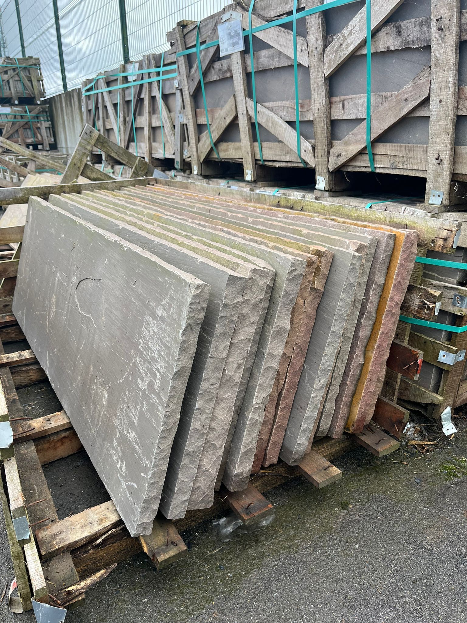 Dalles de béton empilées sur des palettes en bois sur un chantier de construction, cerclées de sangles bleues.