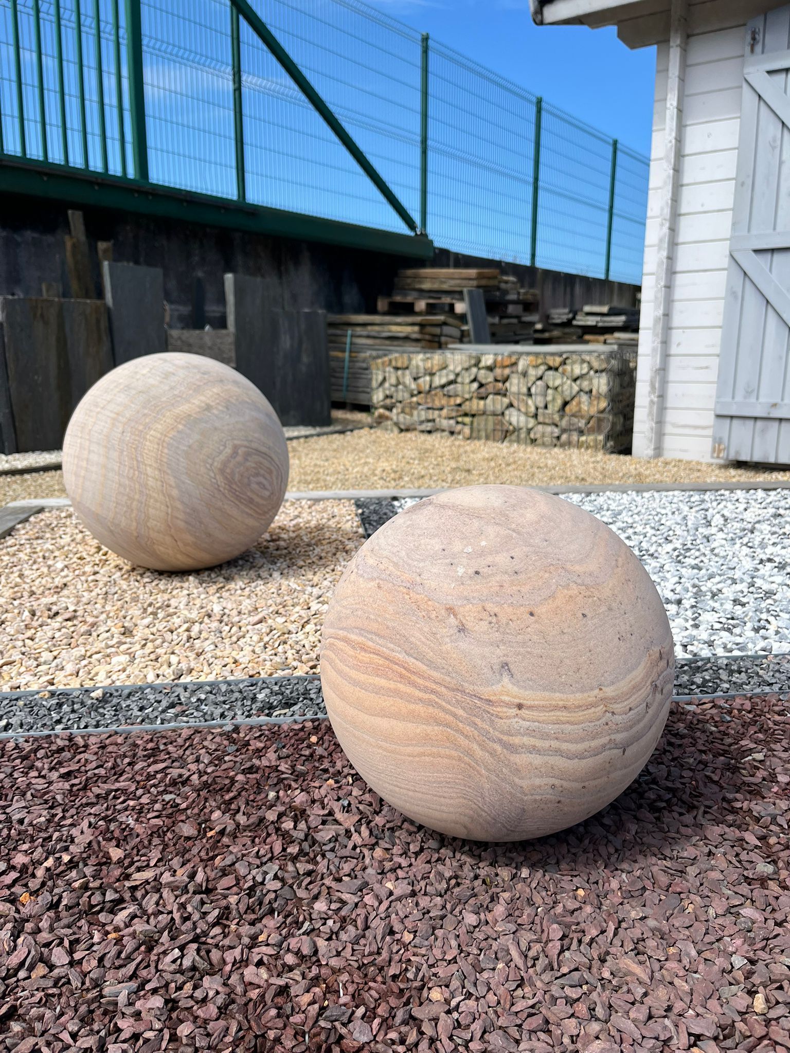 Deux grandes sphères de pierre sur un jardin de gravier, à côté d'un bâtiment blanc et d'une clôture.