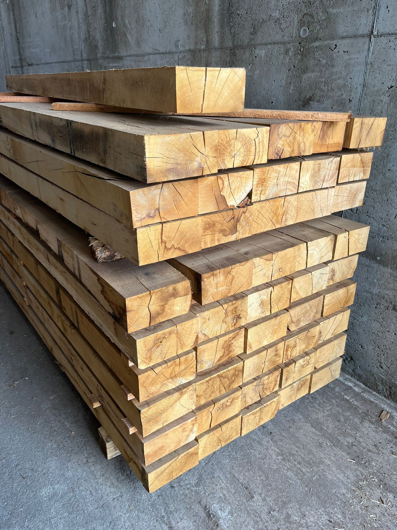 Des planches de bois empilées sur un sol en béton contre un mur gris