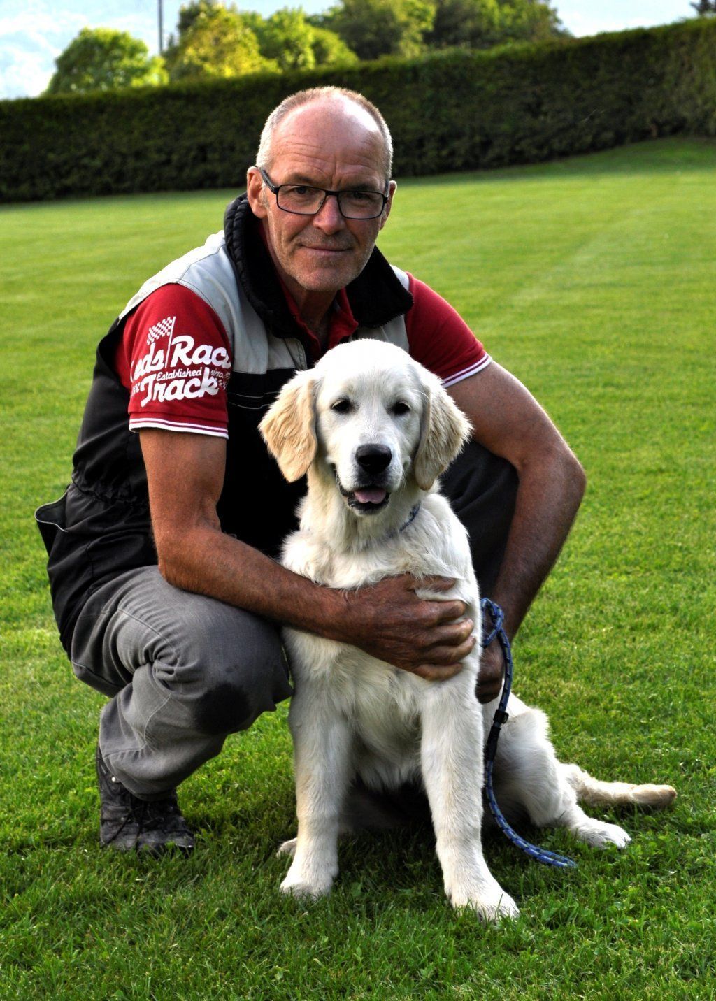 Ein Mann kniet neben einem Golden Retriever-Welpen auf einem Feld. Foto von Zellweger Heini