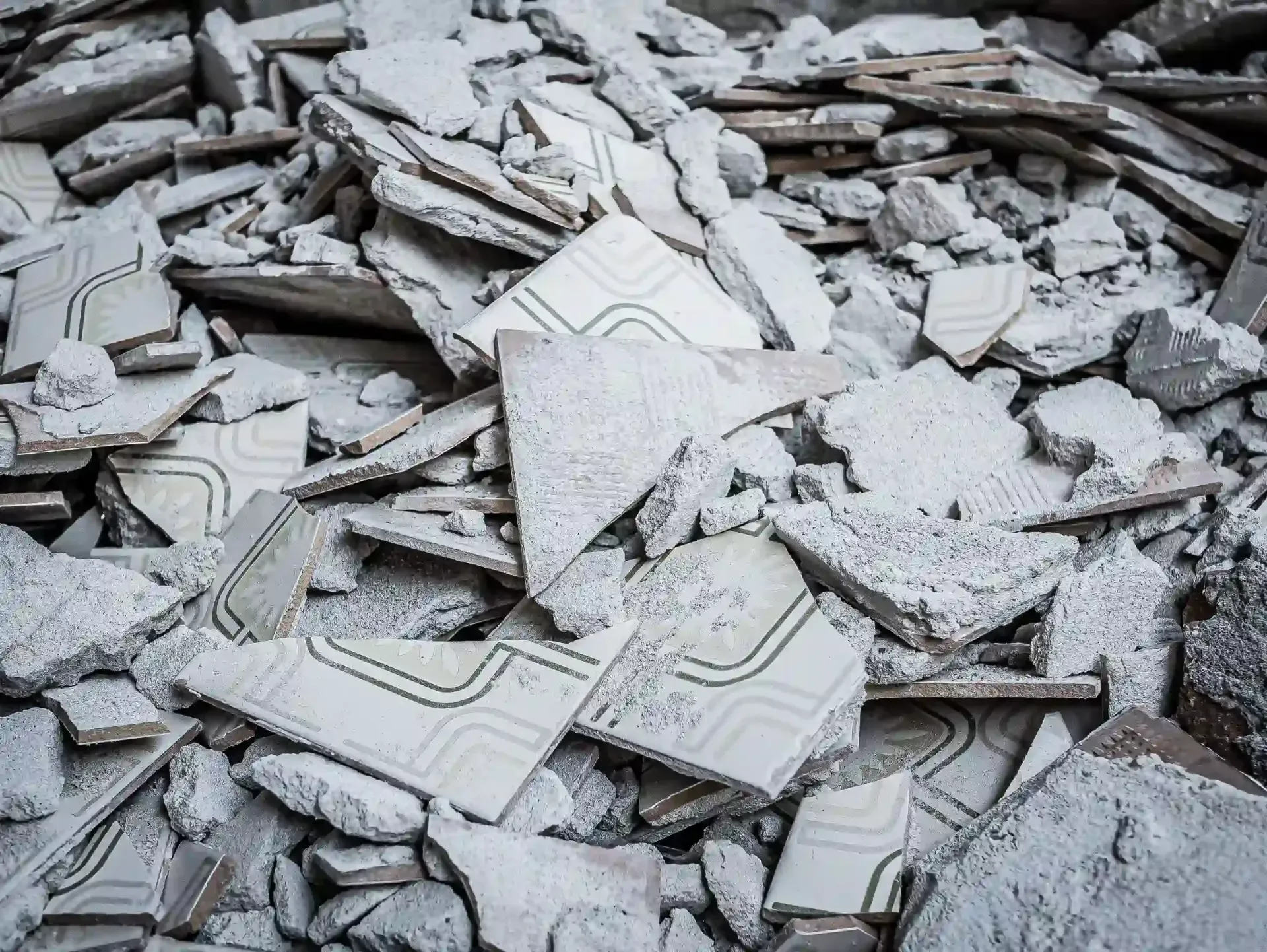 Un montón de baldosas de hormigón rotas con un tenue patrón geométrico repetitivo en tonos grises y blanquecinos.