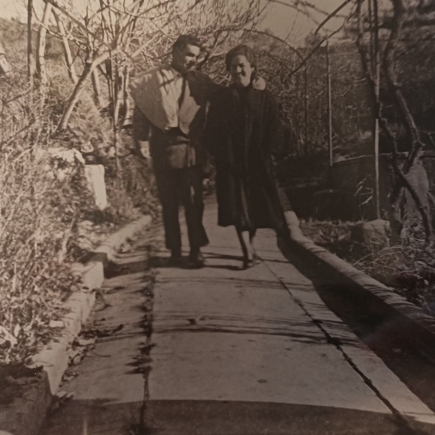 Dos personas caminando del brazo por un sendero estrecho en una zona boscosa.