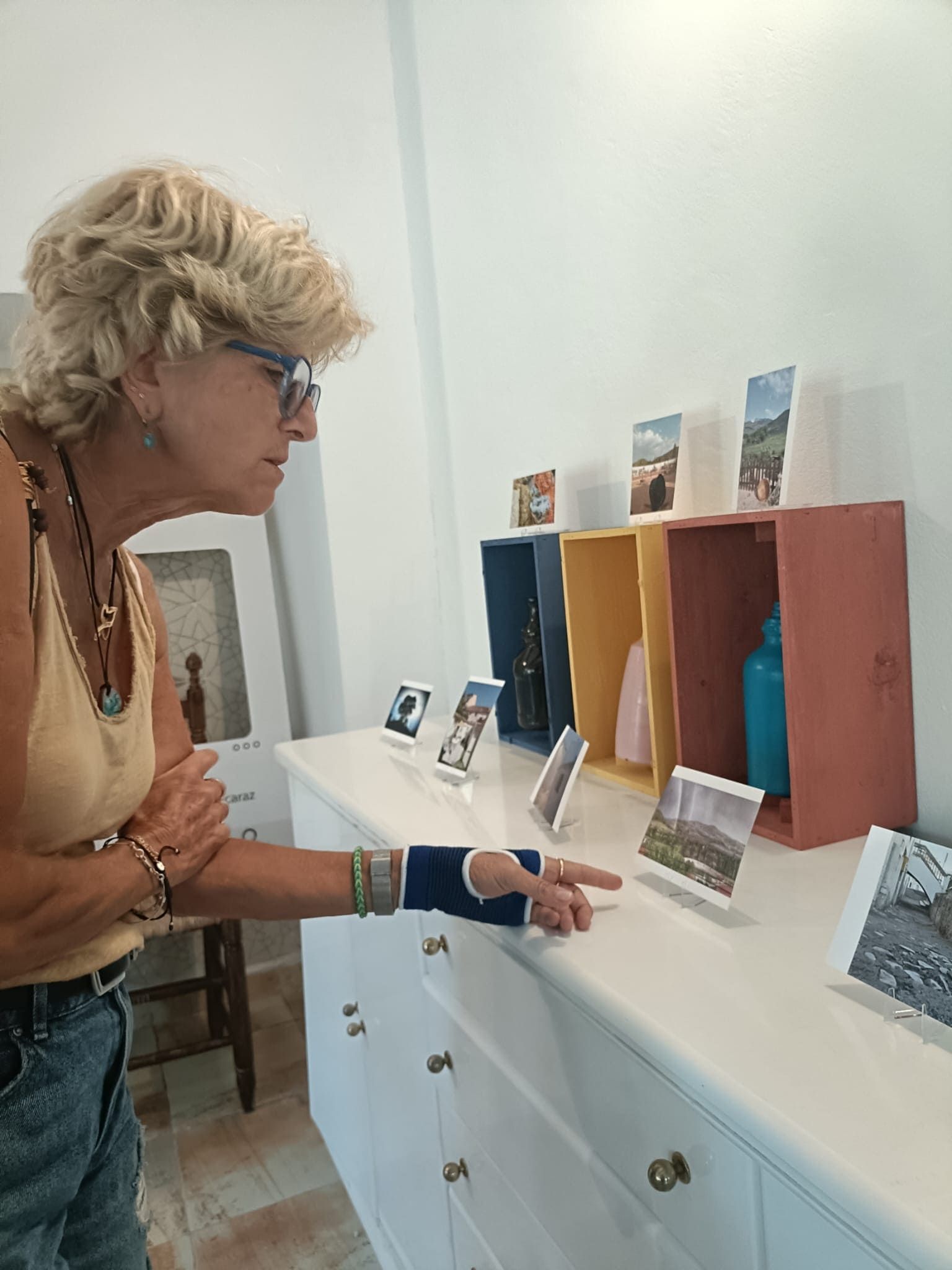 Una persona en una galería examina pequeñas obras de arte expuestas en una vitrina blanca.