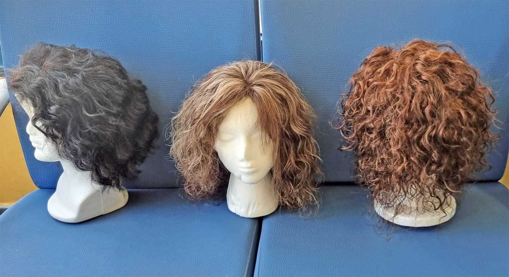 Tres pelucas sobre cabezas de maniquí: negra, marrón medio y marrón rojizo,