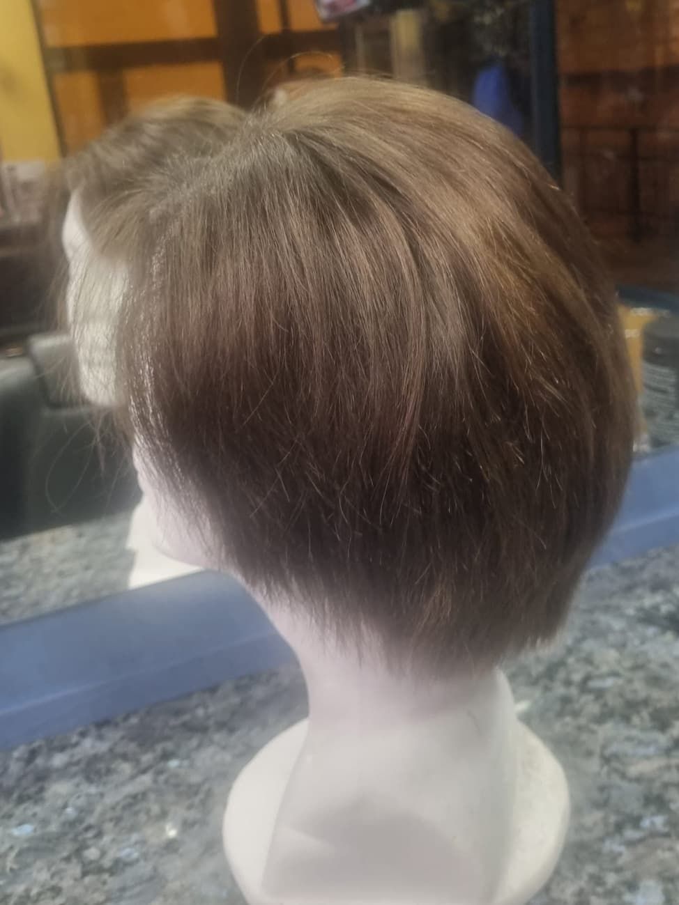 Peluca bob castaña sobre cabeza de maniquí blanca, vista en ángulo. Cabello liso y brillante, con corte corto.