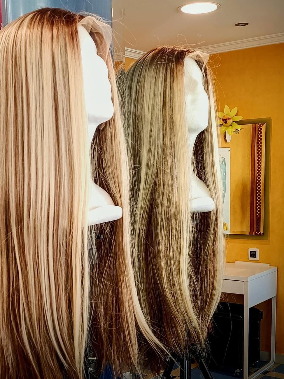 Dos pelucas rubias y castañas sobre cabezas de maniquí blancas en una tienda de pelucas.