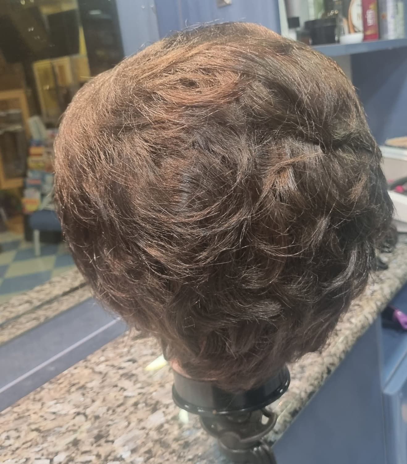 Peluca rizada de color marrón sobre una cabeza de maniquí, colocada sobre un mostrador en un salón.