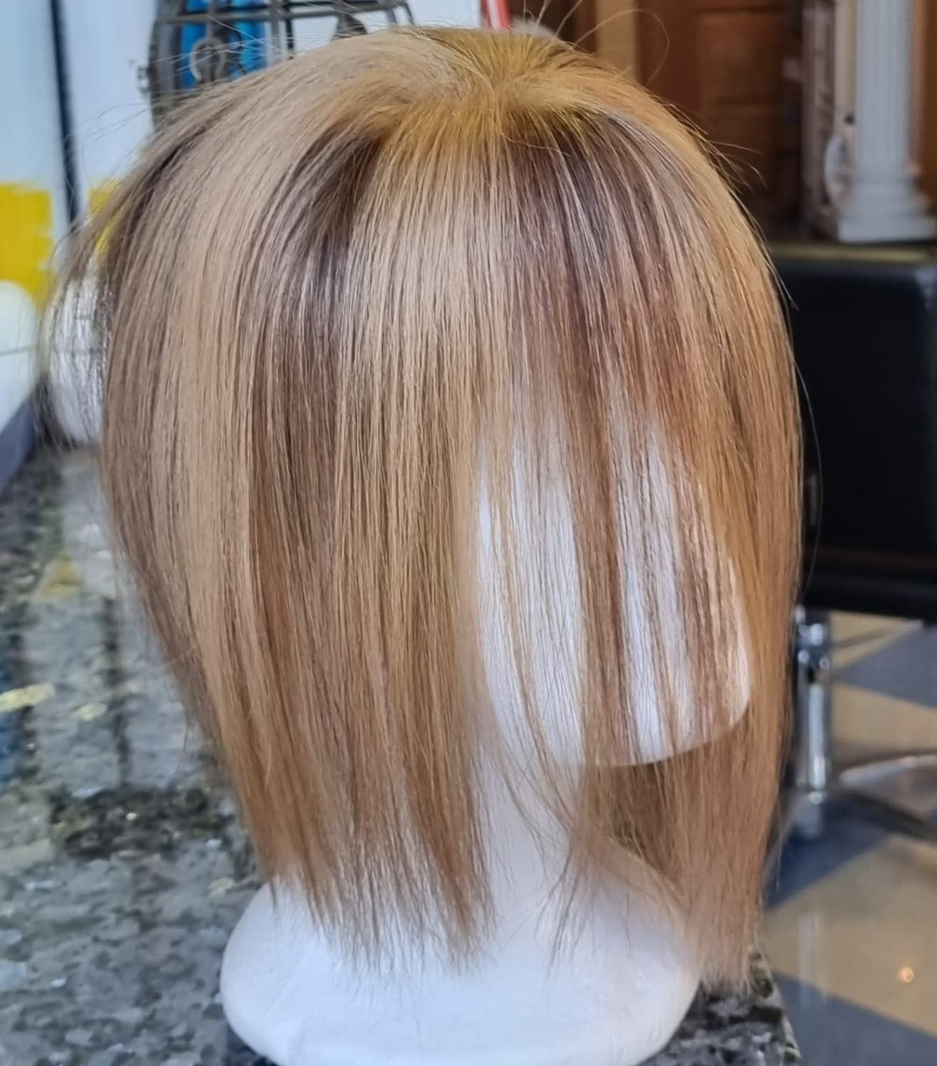 Peluca rubia con reflejos más oscuros sobre una cabeza de maniquí blanca.