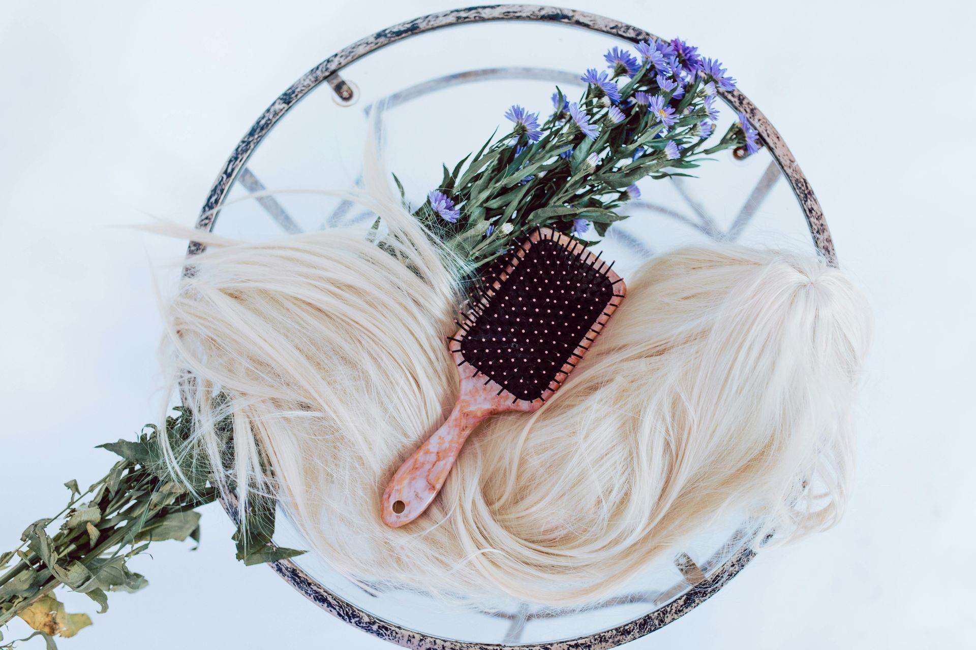 Cabello rubio con un cepillo para el pelo y flores moradas sobre una superficie