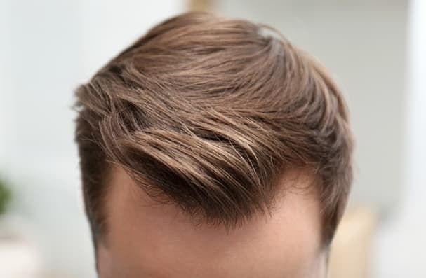 Primer plano de la cabeza de un hombre con cabello castaño y texturizado, peinado hacia un lado.