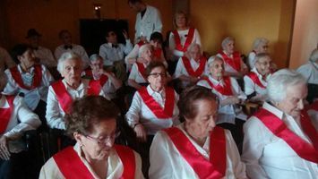 Un grupo de mujeres mayores que llevan fajas rojas están sentadas en una habitación.