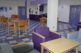 Una sala de estar con sillas y mesas de color morado y un suelo a cuadros.