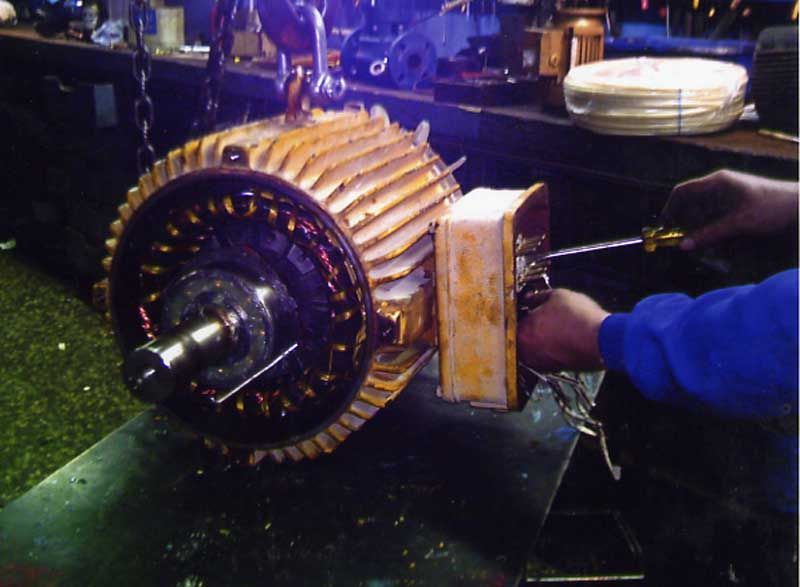 Reparación de motor eléctrico: el técnico utiliza un destornillador en el motor abierto, revelando bobinas internas.