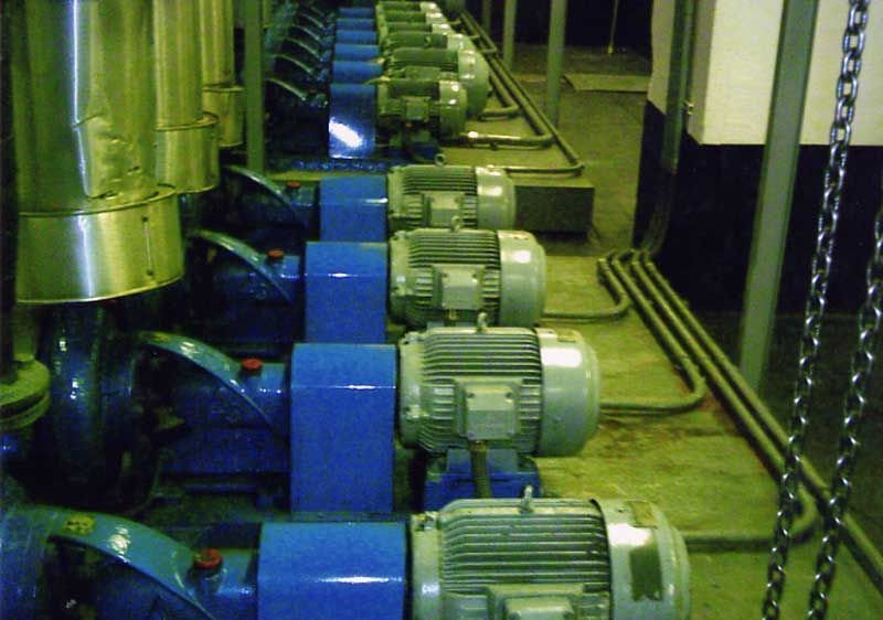 Fila de bombas azules con motores plateados en una sala mecánica, conectadas por tuberías.