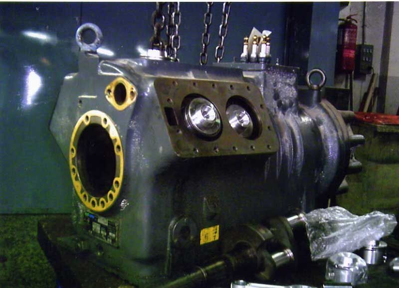 Gran máquina industrial de color gris, con puertos abiertos, suspendida por cadenas.