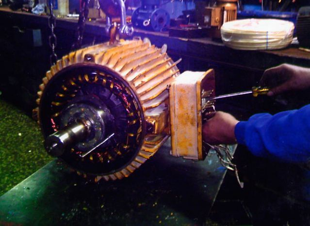 Se está trabajando en un motor eléctrico, sujeto por cadenas. Una persona usa un destornillador para reparar un componente.