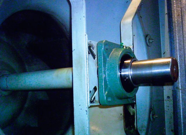 Un eje de metal que se extiende desde una máquina a través de una carcasa de cojinete verde.