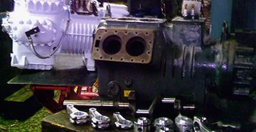 Dos compresores industriales con piezas desmontadas en un banco de trabajo.