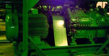 Maquinaria industrial verde, probablemente un compresor, en un entorno interior.