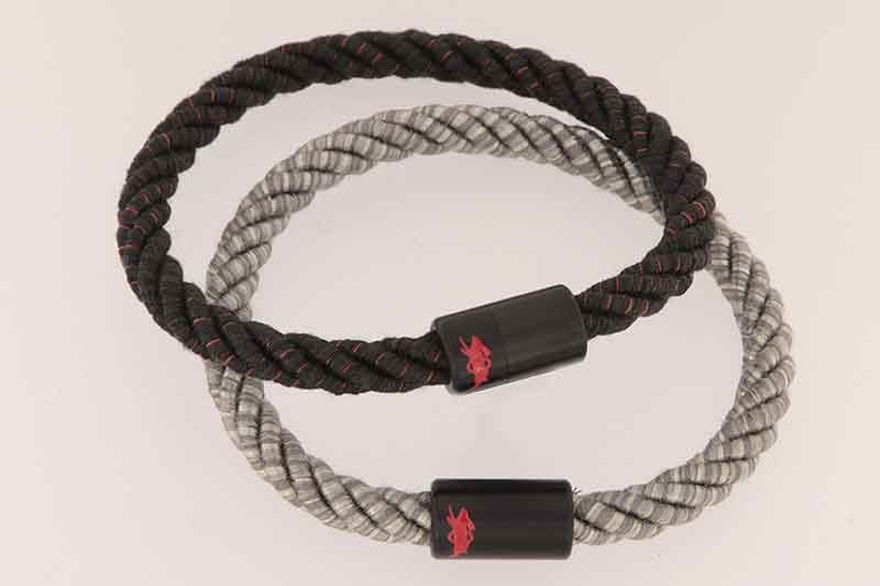 Zwei Seilarmbänder: eines schwarz, eines grau. Beide haben schwarze Verschlüsse mit rotem Text.