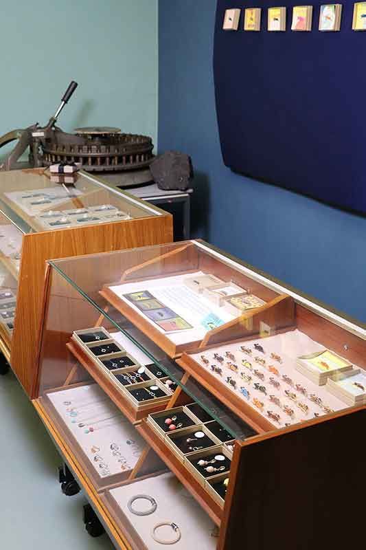 Vitrinen mit Schmuck und einer Druckerpresse in einer Galerieumgebung; blaue Wände.