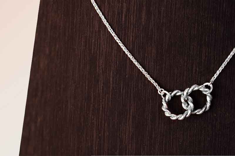 Silberne Halskette mit ineinander verschlungenen Ringen auf dunklem Holzhintergrund.