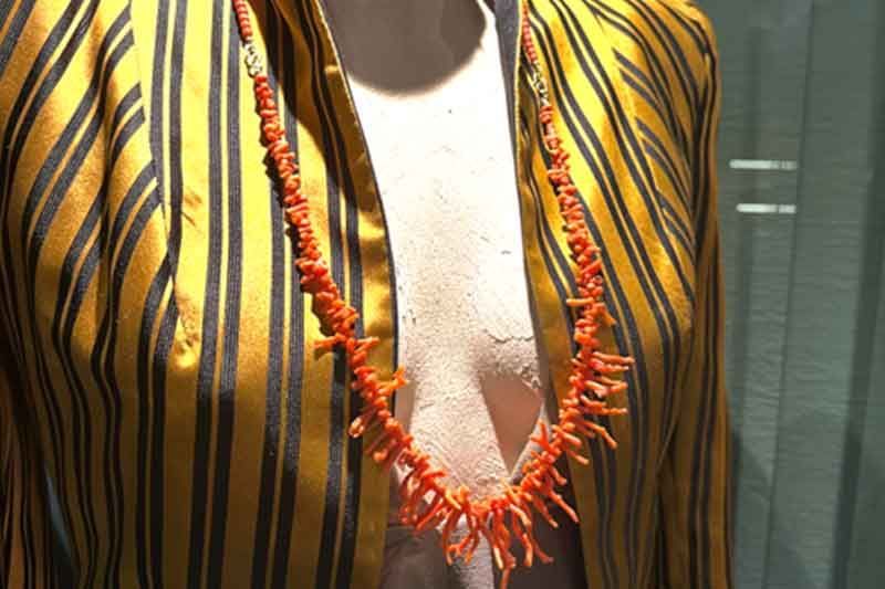 Orangefarbene Korallenkette an einer Schaufensterpuppe, die eine gold-schwarz gestreifte Jacke trägt.