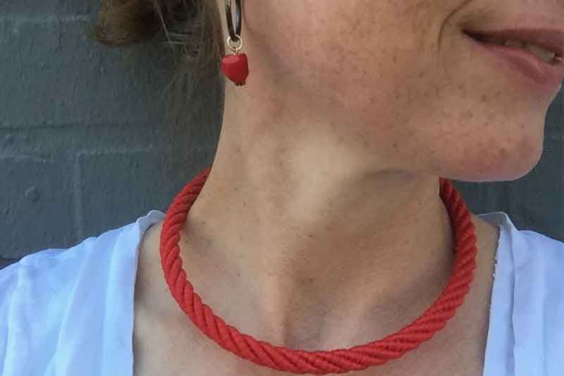 Frau trägt rote Herzohrringe und eine dazu passende Halskette aus gedrehtem Seil.