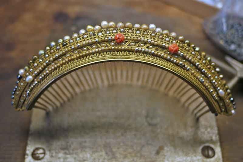 Tiara aus Gold und Perlen mit Korallenakzenten, auf einem Ausstellungsständer.