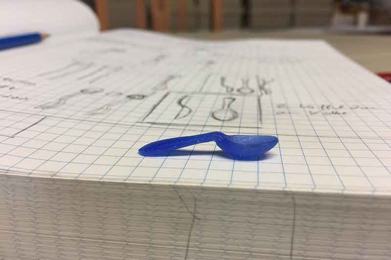 Blaue Plastikschaufel auf einem Notizbuch aus Millimeterpapier, mit Bleistift und Skizzen sichtbar.