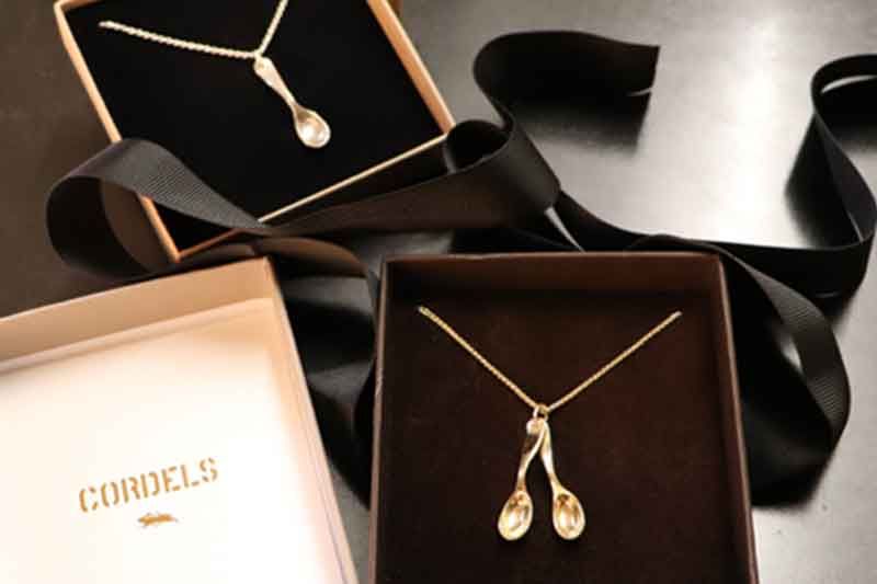 Zwei goldene Halsketten mit Löffelanhängern in Schmuckschatullen mit schwarzen Bändern.