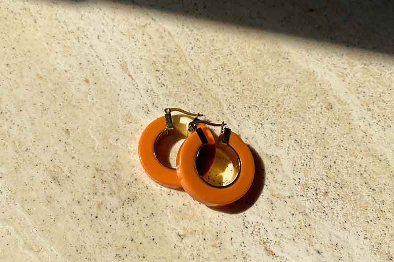 Orangefarbene Creolen auf heller, strukturierter Oberfläche; Sonnenlicht wirft einen Schatten.